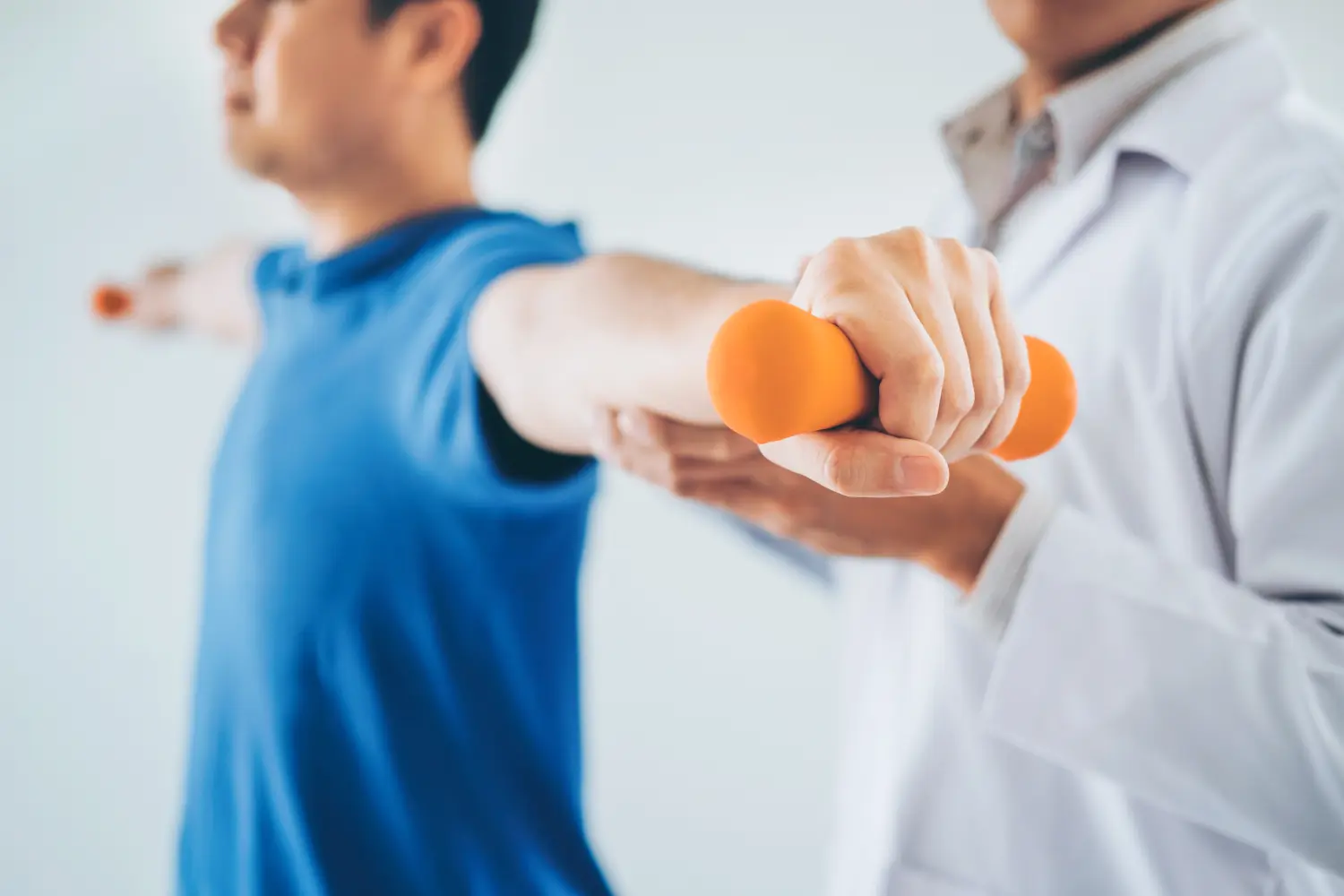 Physiotherapeut-Mann gibt Übung mit Hantelbehandlung über Arm und Schulter eines männlichen Athleten-Patienten Physiotherapie-Konzept